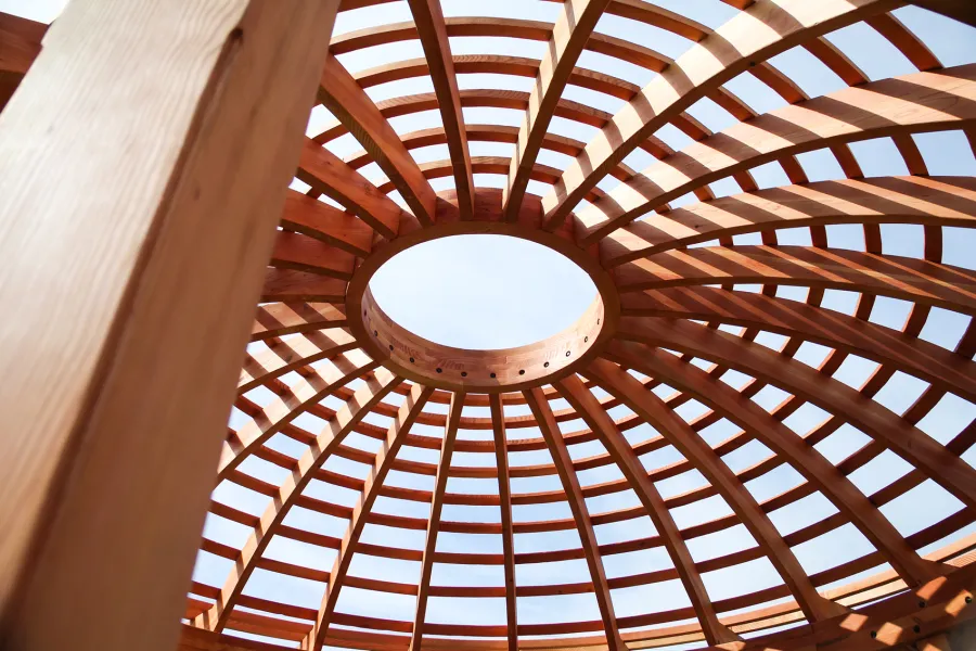 Wooden Dome Pergola (Options: 16' Diameter, with Deck in Coffee Stain, Douglas-fir, Open Roof with Slats at 6", 9' Posts, No Electrical Wiring Trim, 6-Post Anchor Kit for Concrete, Transparent Premium Sealant). Photo Also shows a Round Picnic Table and a Rory's Swing Set in Background.
