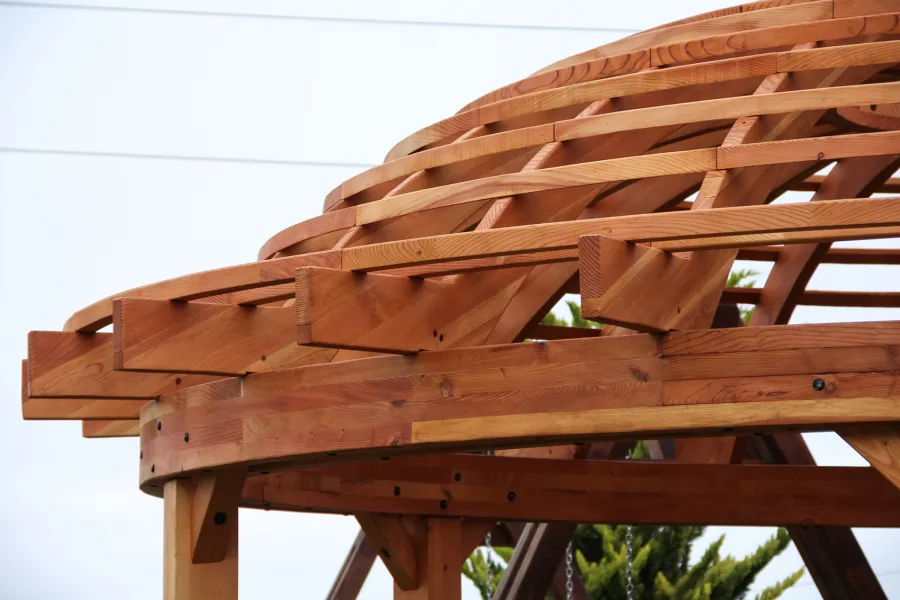 Wooden Dome Pergola (Options: 16' Diameter, with Deck in Coffee Stain, Douglas-fir, Open Roof with Slats at 6", 9' Posts, No Electrical Wiring Trim, 6-Post Anchor Kit for Concrete, Transparent Premium Sealant). Photo Also shows a Round Picnic Table and a Rory's Swing Set in Background.