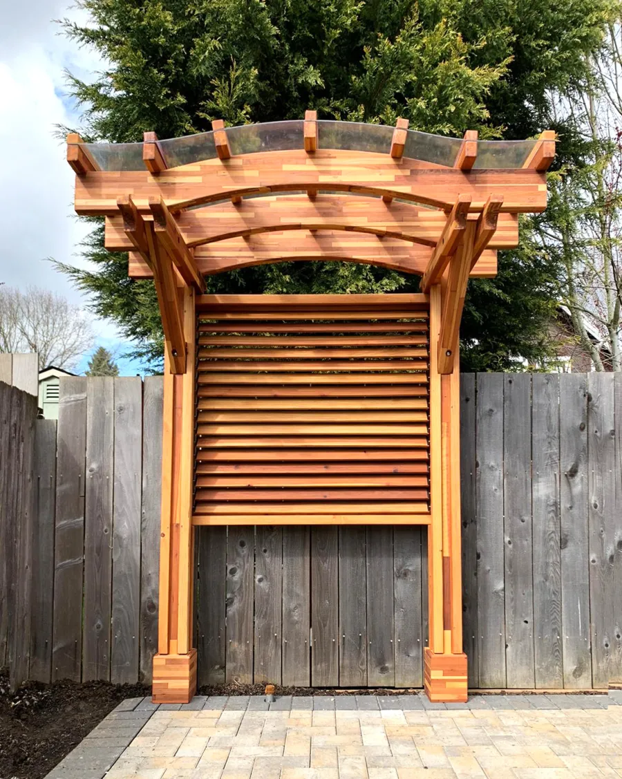 Two-Post Arched Wood Arbor (Options: 6' x 3', Mosaic Redwood, 7' Posts Height, 2-Post anchor Kit for High-Wind, Custom Louvered Half Height Privacy Wall Added by Customer Request, Vertical Post Decorative Trims, with Rain Guard, Transparent Premium Sealant). Photo Courtesy of E. Baechler of Portland, Oregon.