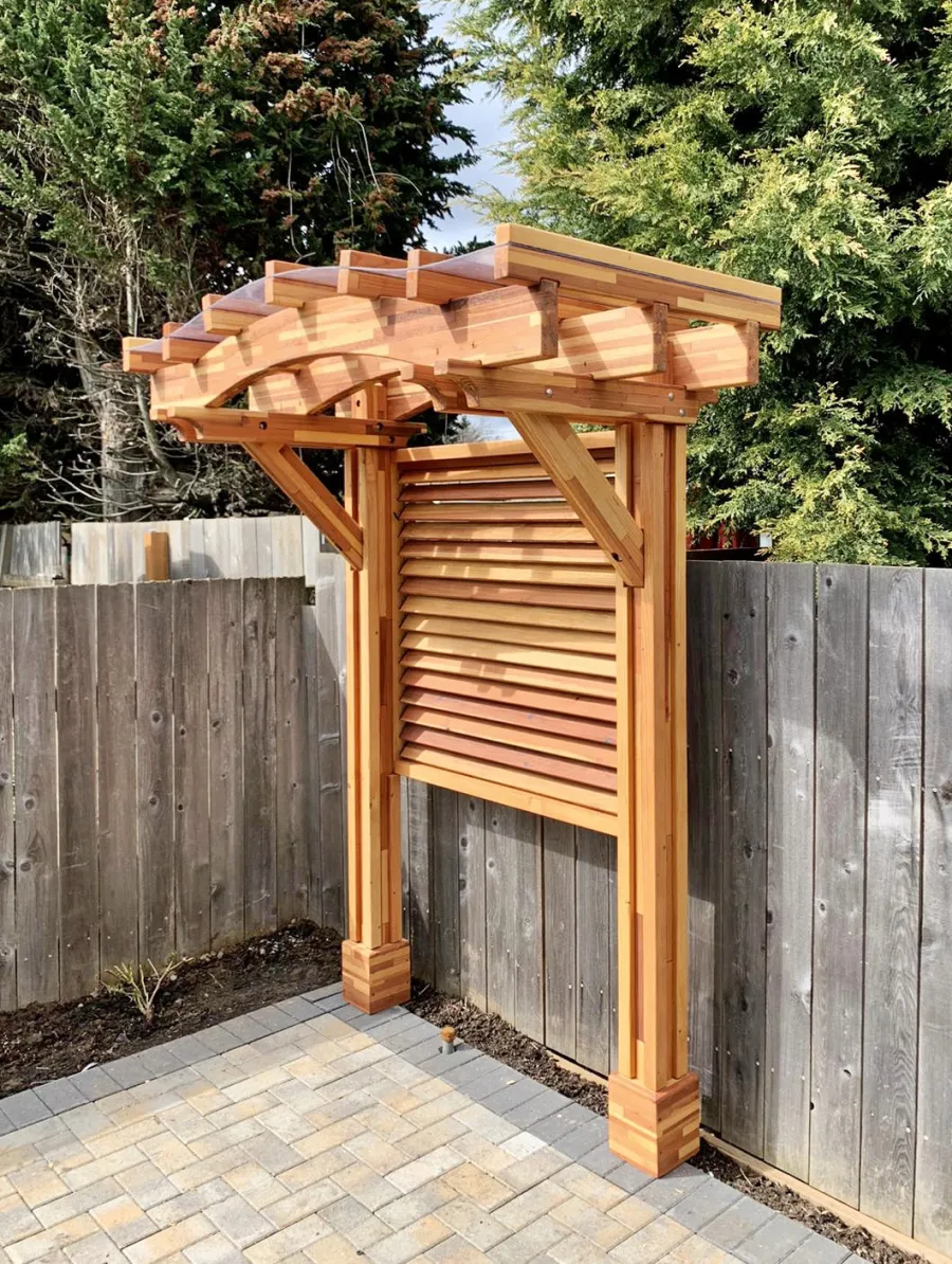 Two-Post Arched Wood Arbor (Options: 6' x 3', Mosaic Redwood, 7' Posts Height, 2-Post anchor Kit for High-Wind, Custom Louvered Half Height Privacy Wall Added by Customer Request, Vertical Post Decorative Trims, with Rain Guard, Transparent Premium Sealant). Photo Courtesy of E. Baechler of Portland, Oregon.