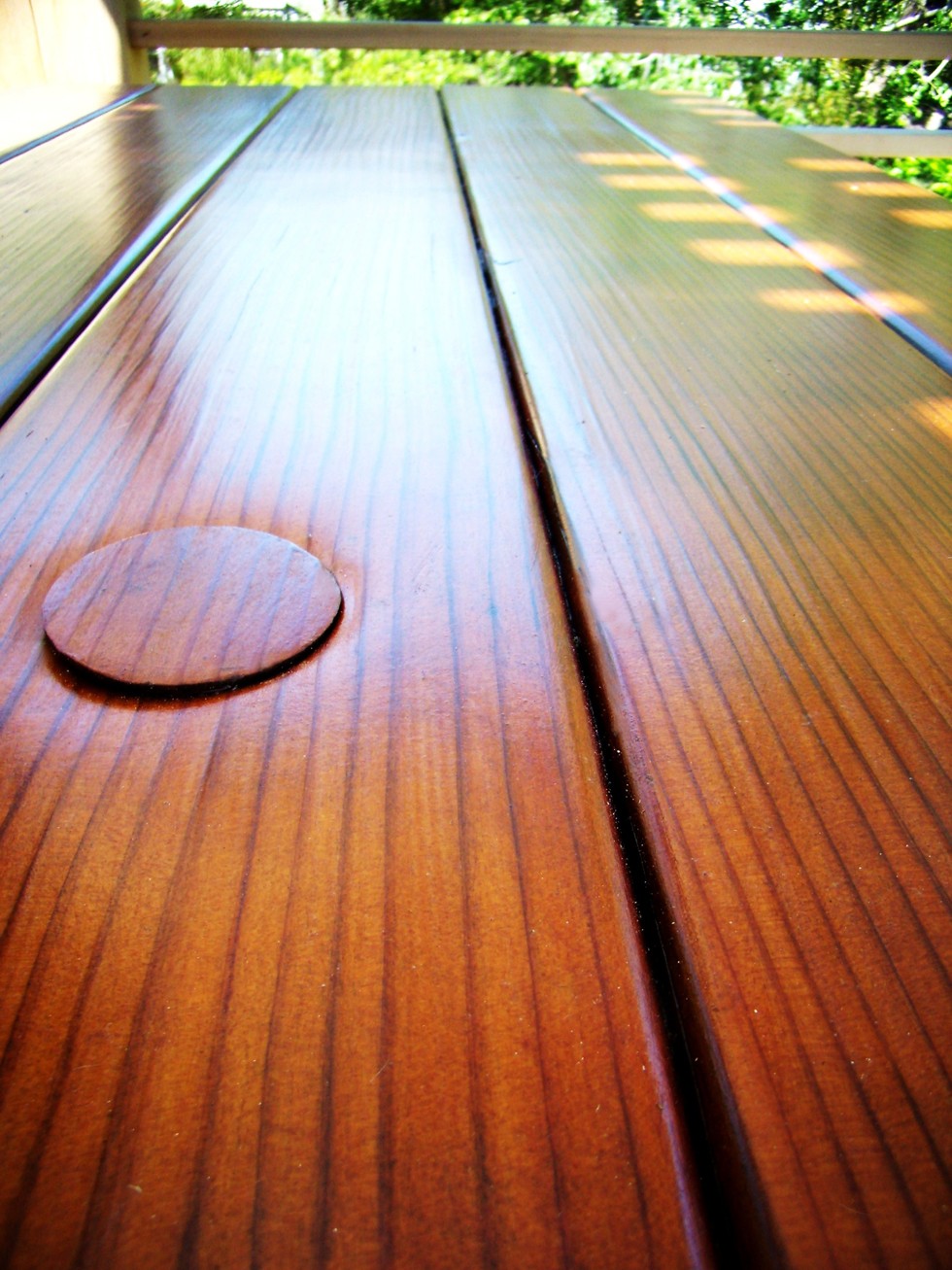 Closeup of tabletop highlighting the quality of the vertical grain lumber and the Transparent Premium Sealant - Mature Redwood. Umbrella hole and plug is shown on top left.