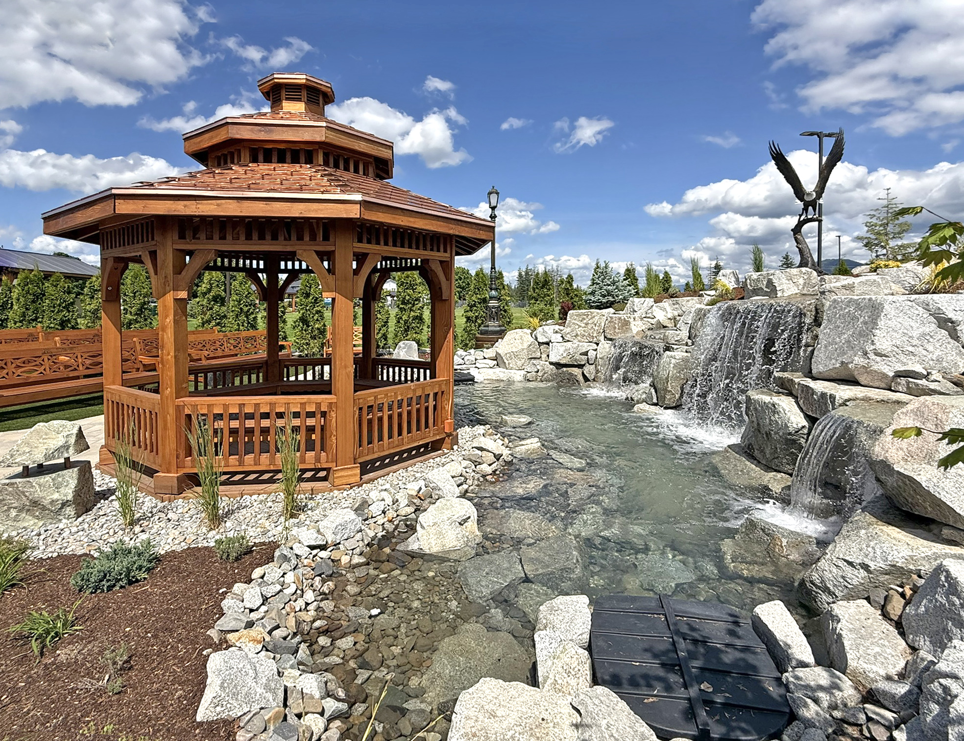 Custom Octagonal Pavilion (Options: 14' Diameter, Mature Redwood, 8' H Posts, 6x6 Posts, with Seating Area Under the Pavilion, Post Anchor Kit for High-Wind, Transparent Premium Sealant). Photo Also Shows Some Hennell Benches. Installed in Faith Walk Community Fitness Park in Coeur d'Alene, Idaho.